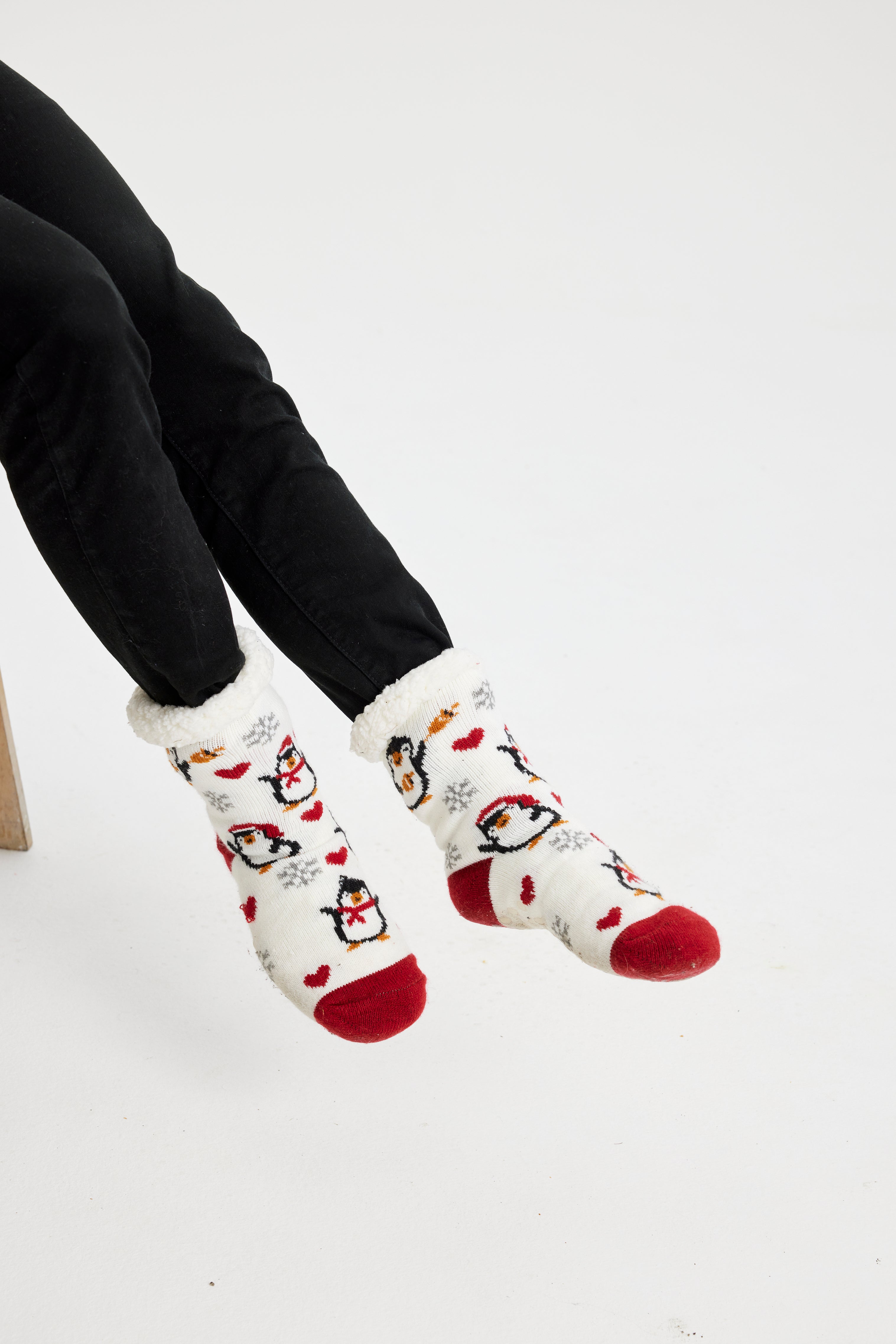 Ein Paar Beine, die ein Paar rote und weiße Weihnachtssocken mit Pinguinen darauf tragen.